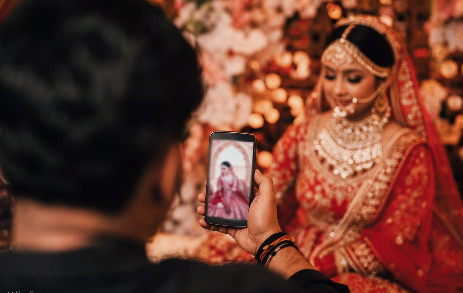 Phone showing a pose card in the library, bride blurred in warm mandap light behind it